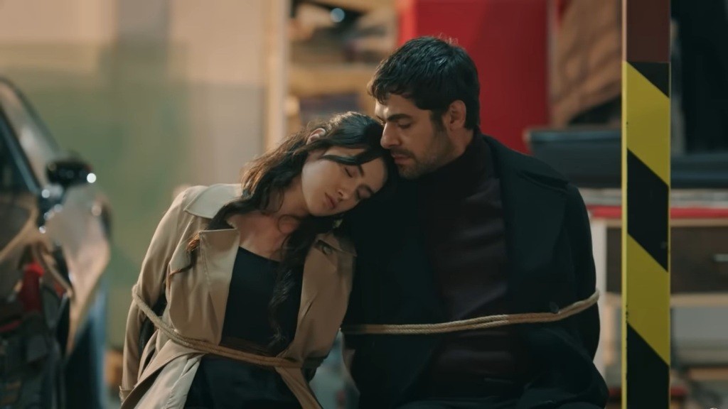 Halil i Zeynep są przywiązani do krzeseł. Zeynep zasnęła, kładąc głowę na jego ramieniu.