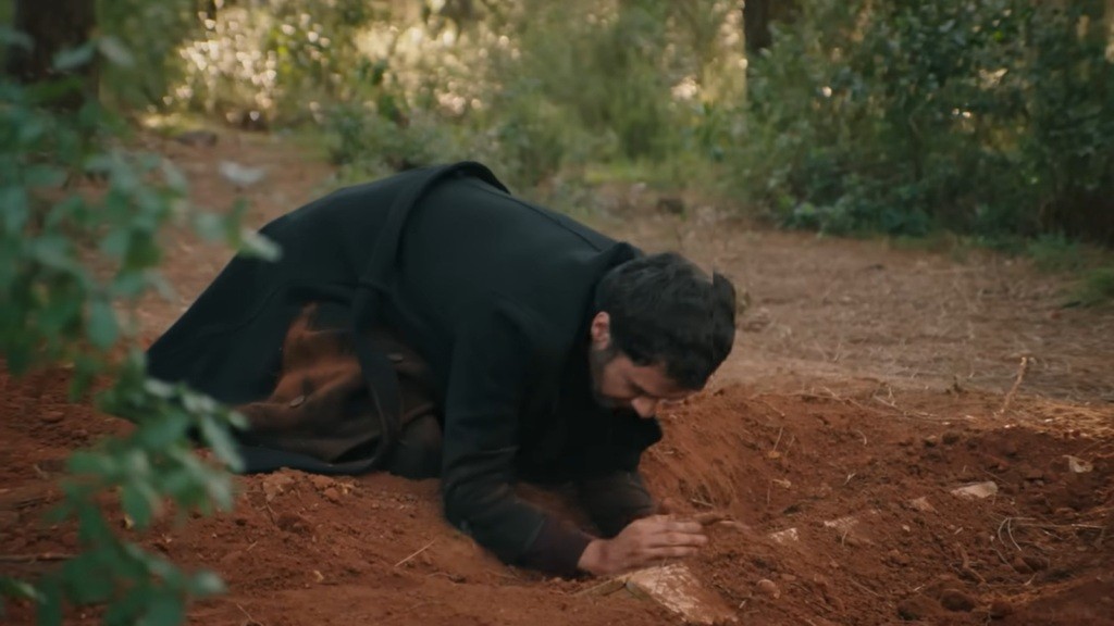 Halil rozgrzebuje ziemię, odsłaniając pokrywę trumny.