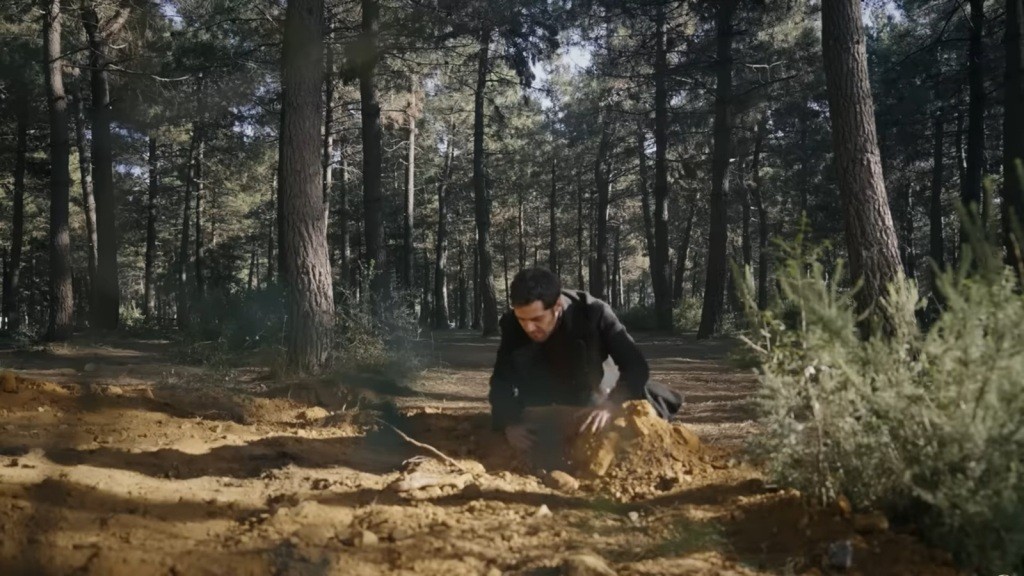 Halil rękoma odrzuca ziemię z nagrobka w lesie.