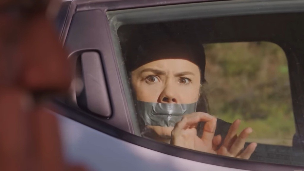 Porwana Gonul wygląda przez boczną szybę samochodu. Ma zaklejone taśmą usta i związane ręce.
