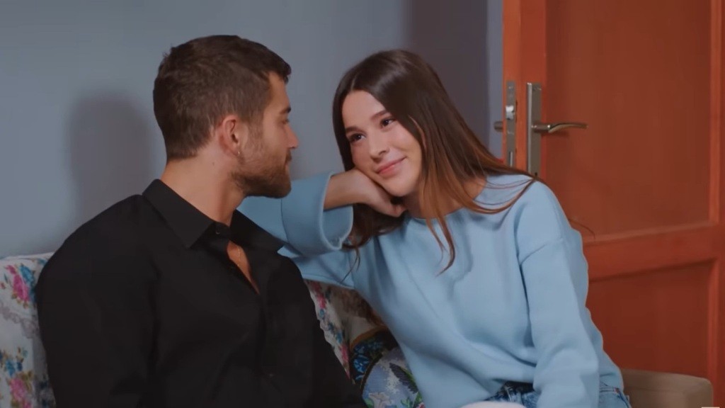 Cihan i Zeynep siedzą na wersalce. Ona opiera policzek na dłoni i patrzy na niego zalotnie.
