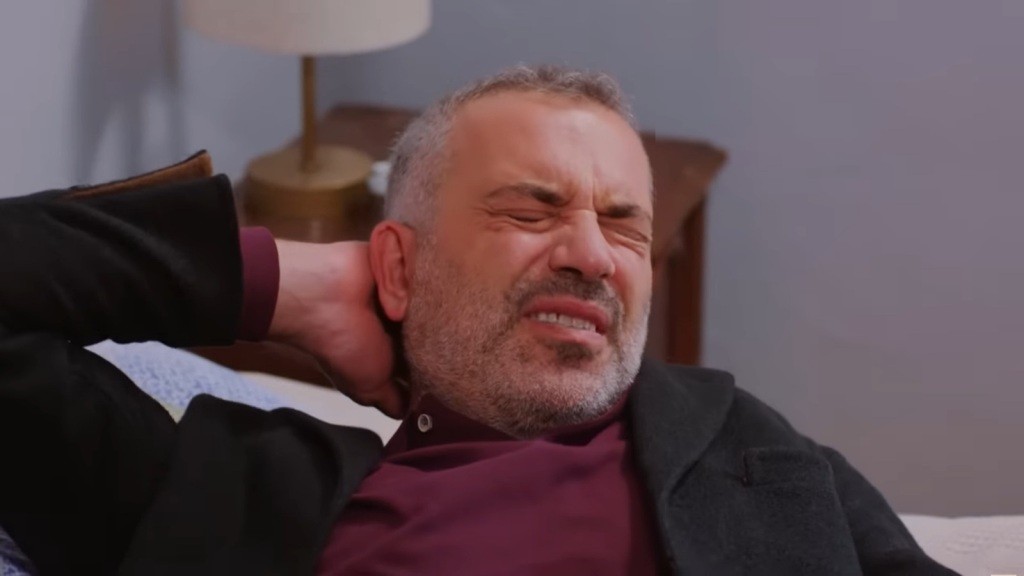 Bulent mruży oczy, a na jego twarzy maluje się grymas bólu. Trzyma się za potylicę.