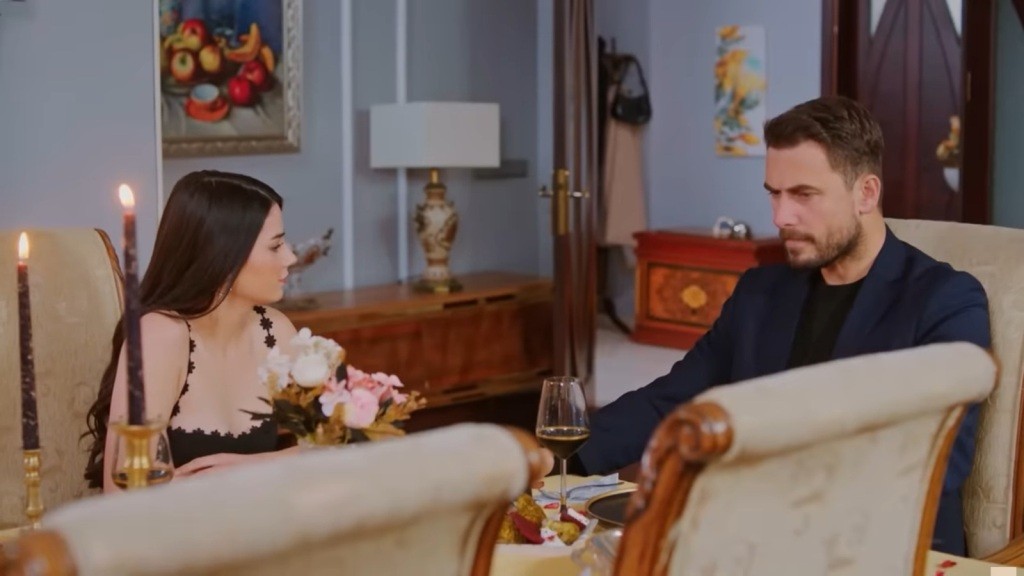 Bahar i Kuzey siedzą przy stole, na którym palą się dwie wysokie świeczki.