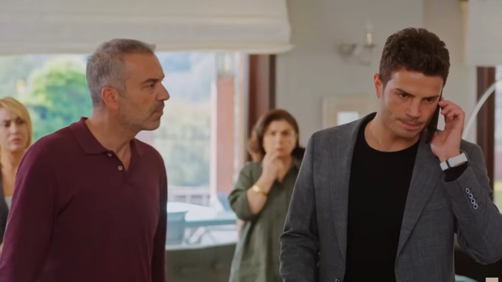 Ege rozmawia przez telefon. Obok niego stoi Bulent, a za nim Naciye.