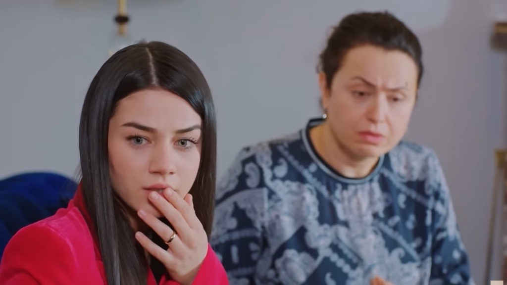 Bahar dotyka ust palcami, wyraźnie przestraszona. Obok niej siedzi jej mama.