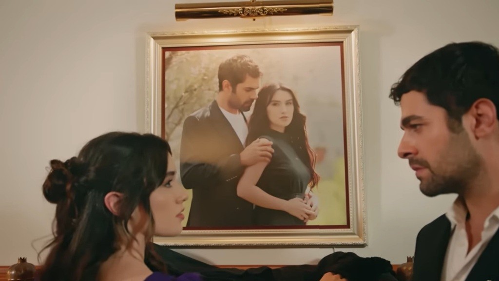 Zeynep i Halil stoją obok ściany, na której wisi ich zdjęcie.