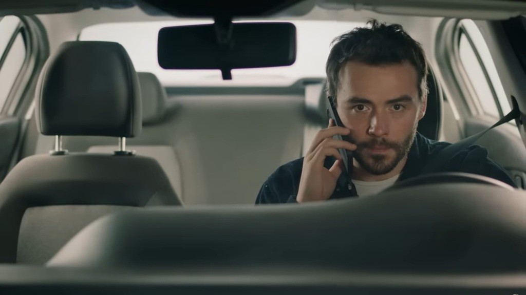 Hakan rozmawia przez telefon, siedząc za kierownicą.