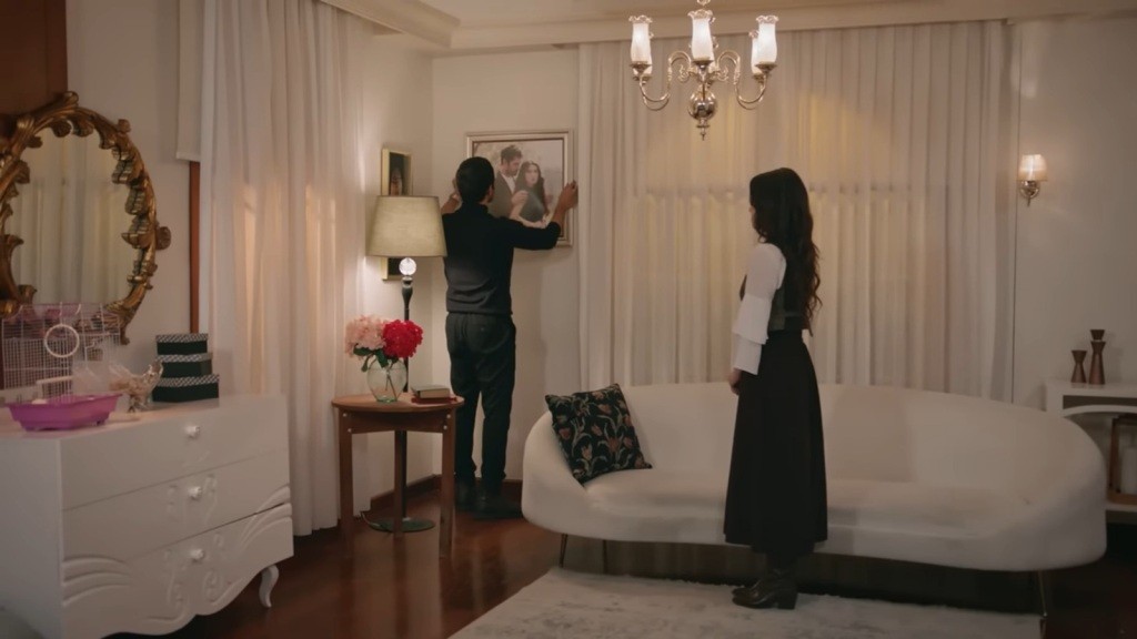 Halil wiesza oprawione w ramkę zdjęcie na ścianie.