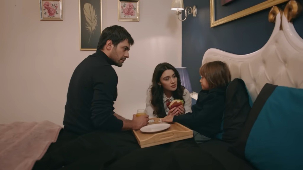 Zeynep podaje leżącemu w łóżku Ardzie burgera.