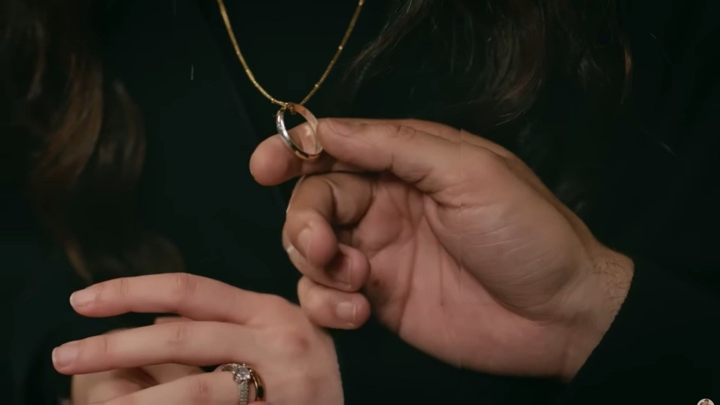 Halil trzyma w palcach zawieszoną na łańcuszku obrączkę.