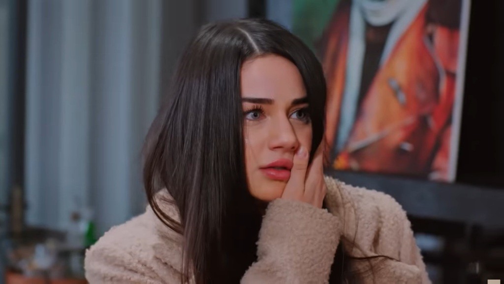 Bahar trzyma się za policzek.