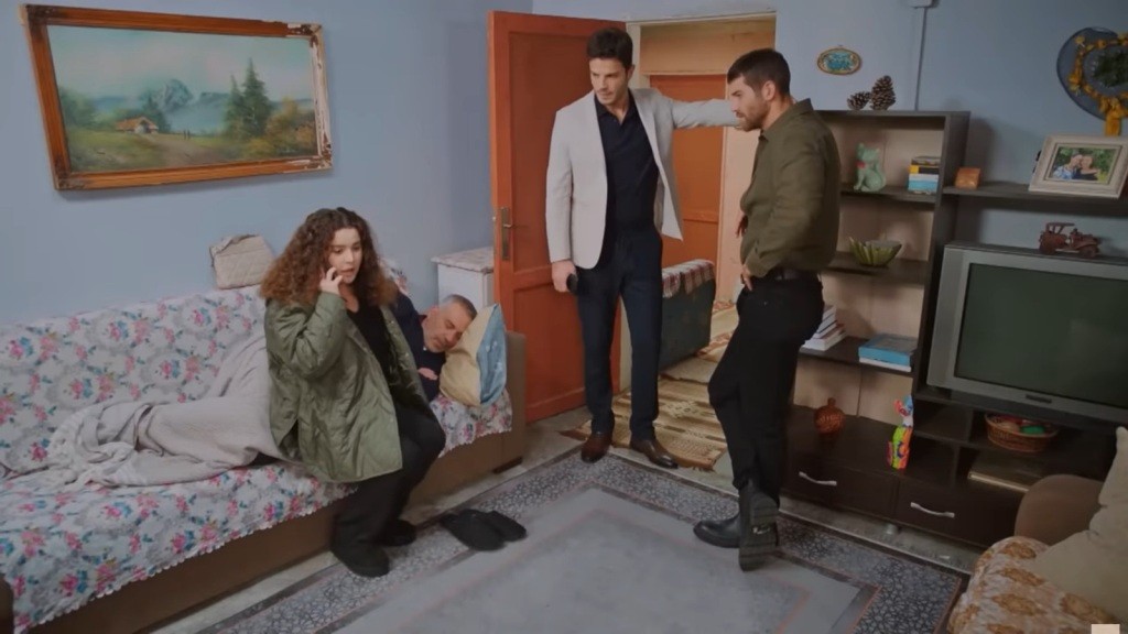 Melis rozmawia przez telefon, siedząc na skraju wersalki, na której śpi jej ojciec. W pokoju stoją Ege i Cihan.