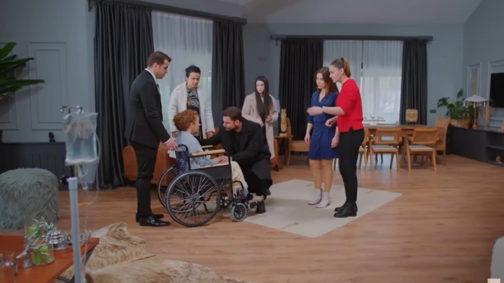Kuzey kuca przed wózkiem inwalidzkim, na którym siedzi jego siostra. Wokół zgromadzeni są: Husnu, Cavidan, Bahar, Yildiz i Hulya.