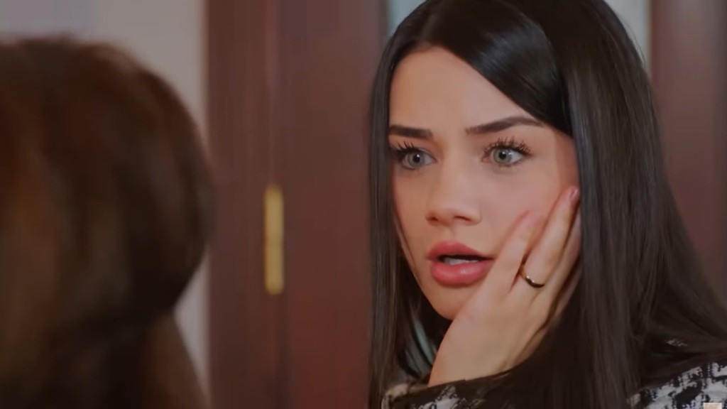 Bahar trzyma się za policzek.