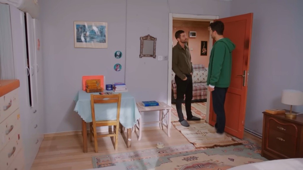 Cihan opiera się o framugę i patrzy na Egego, który wszedł do pokoju w domu Gonul. Drzwi szafy są lekko uchylone.