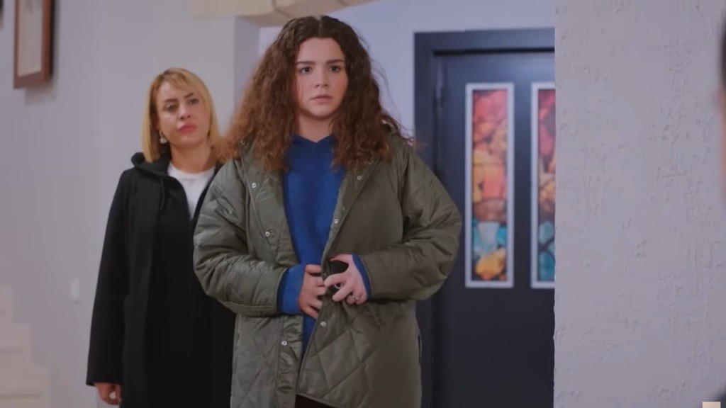 Melis trzyma ręce na brzuchu, stojąc w przedpokoju. Za nią stoi Belkis.