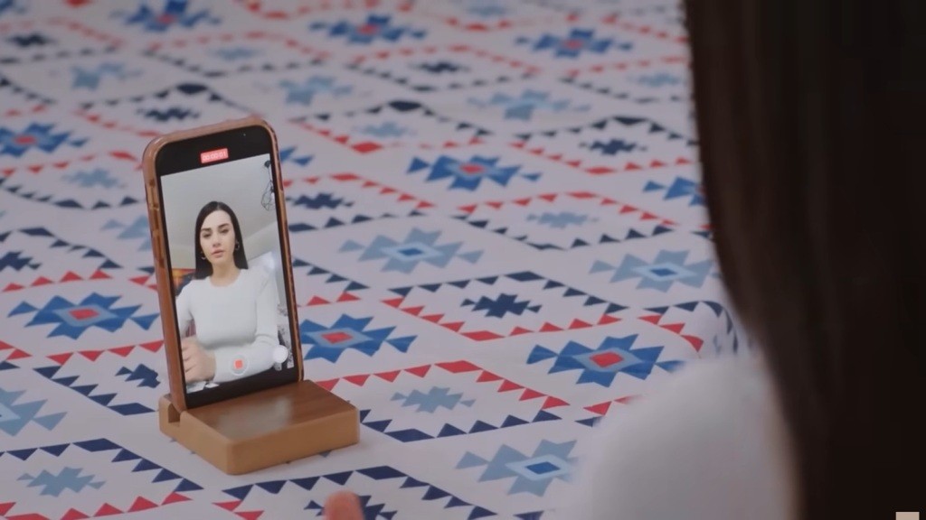 Telefon z włączonym nagrywaniem, przed którym siedzi Bahar.