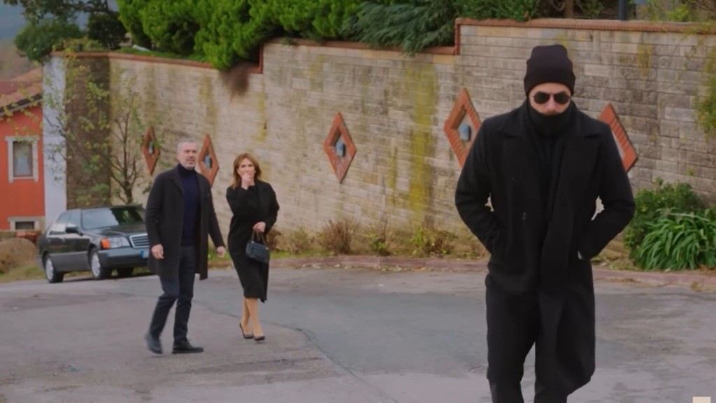 Ubrany na czarno Kuzey idzie drogą. Bulent i Feraye skupiają na nim wzrok, stojąc około dziesięć metrów dalej.