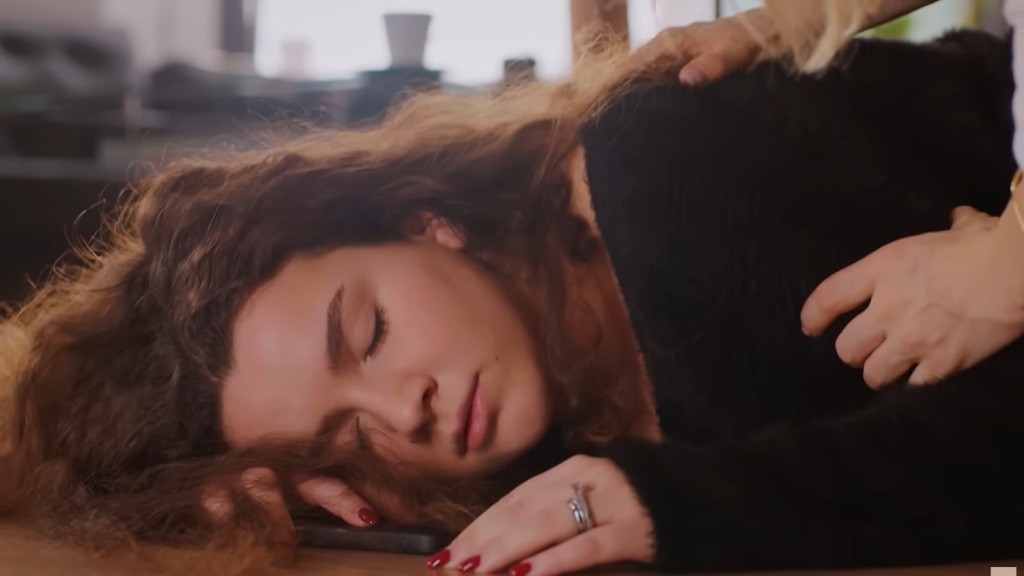 Zbliżenie na twarz nieprzytomnej Melis, która leży na podłodze, z policzkiem przytulonym do paneli.