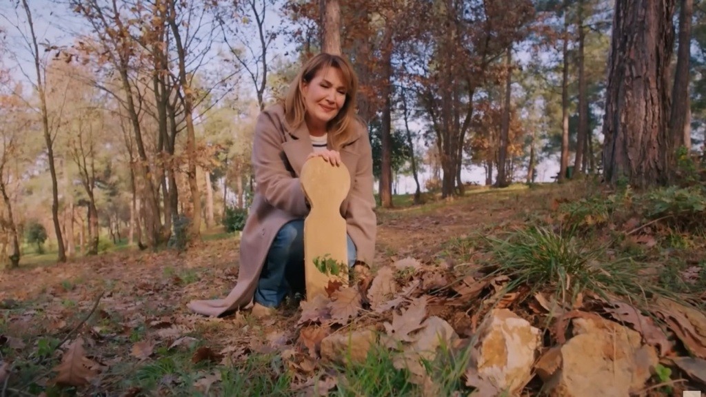 Feraye klęczy przy grobie w lesie, a na jej twarzy maluje się wyraz głębokiej rozpaczy.