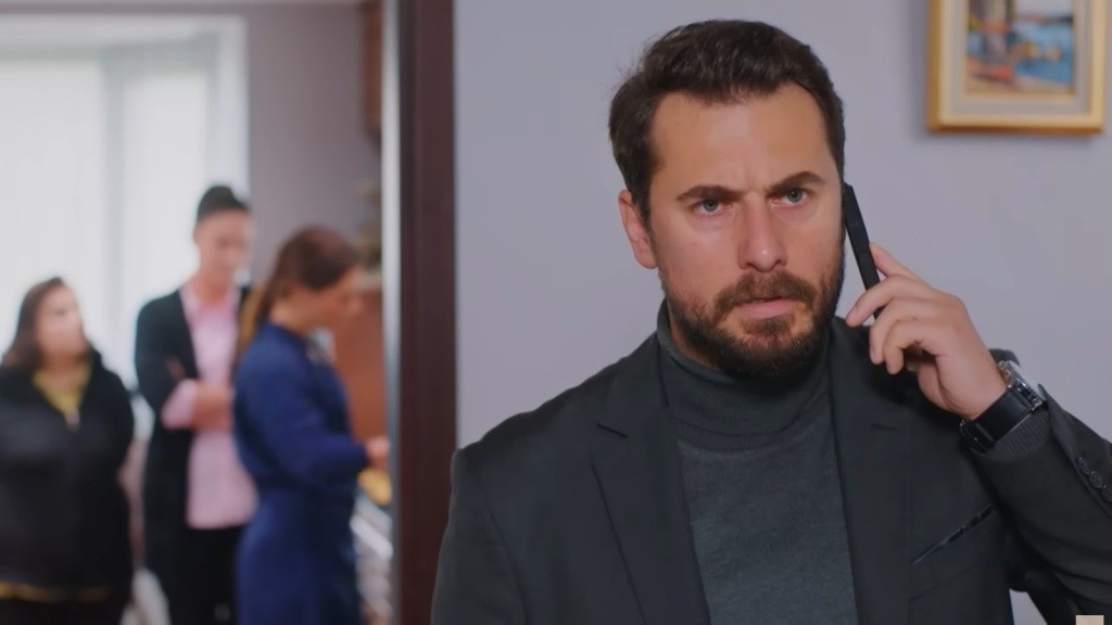 Kuzey rozmawia przez telefon. Za jego plecami znajduje się pokój, a w nim zamglone sylwetki Naciye, Yildiz i Sili.