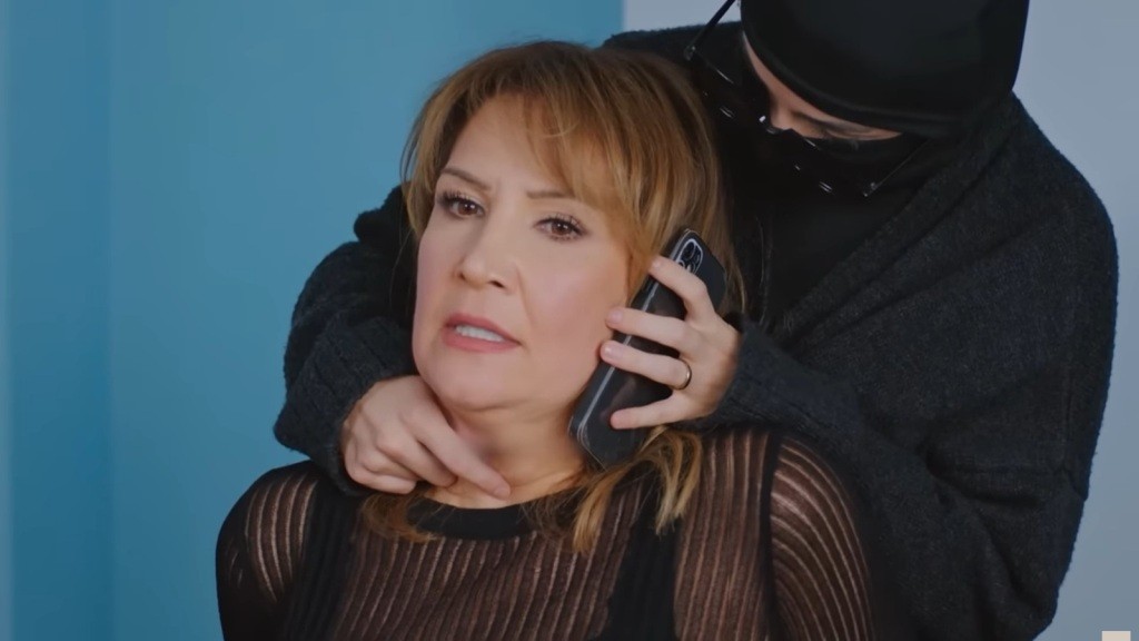 Zamaskowana postać trzyma telefon przy policzku Feraye, zmuszając ją do rozmowy.