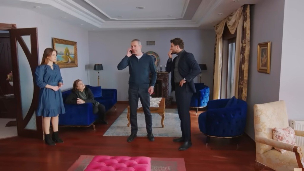 Naciye siedzi na kanapie. W wejściu do salonu stoi Sila. Bulent rozmawia przez telefon, a obok niego stoi Kuzey.