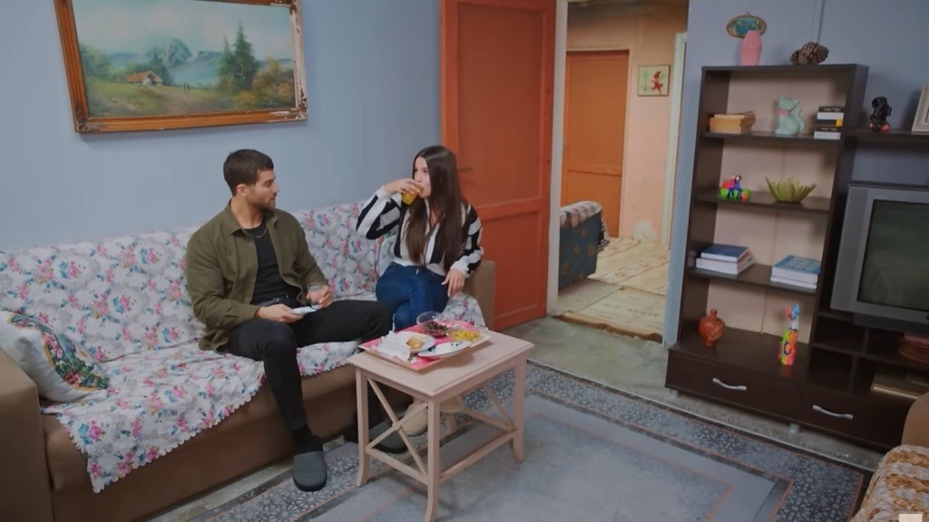 Cihan i Zeynep siedzą na wersalce. On przygląda się uważnie, jak ona pije sok pomarańczowy.