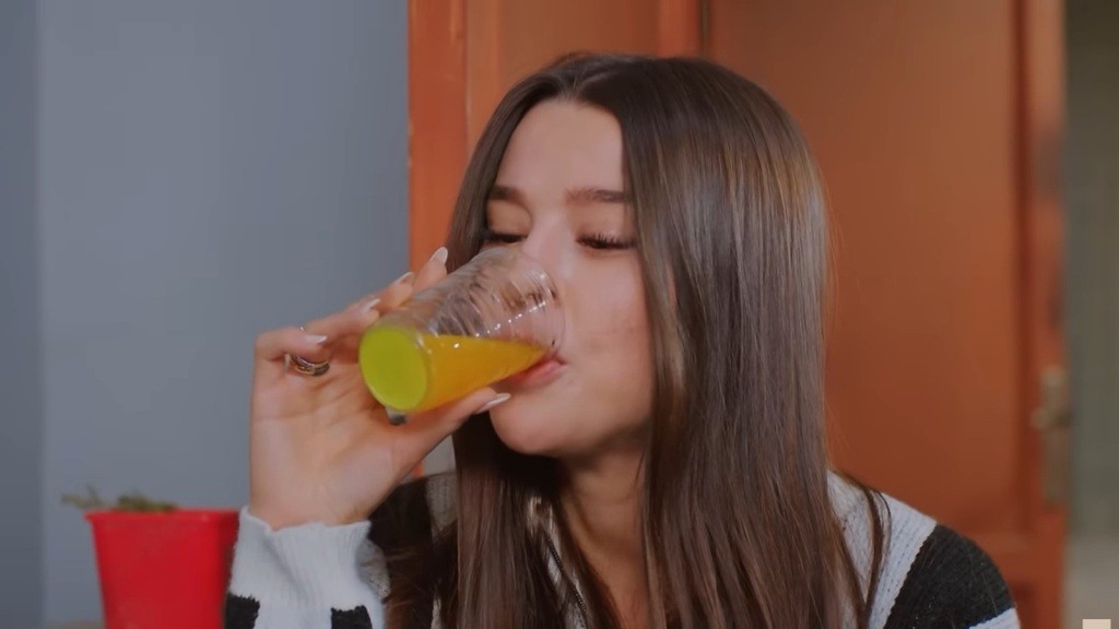 Zeynep przechyla szklankę, pijąc sok pomarańczowy.