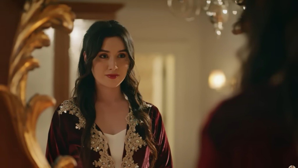 Zeynep stoi przed lustrem, lekko się uśmiechając.