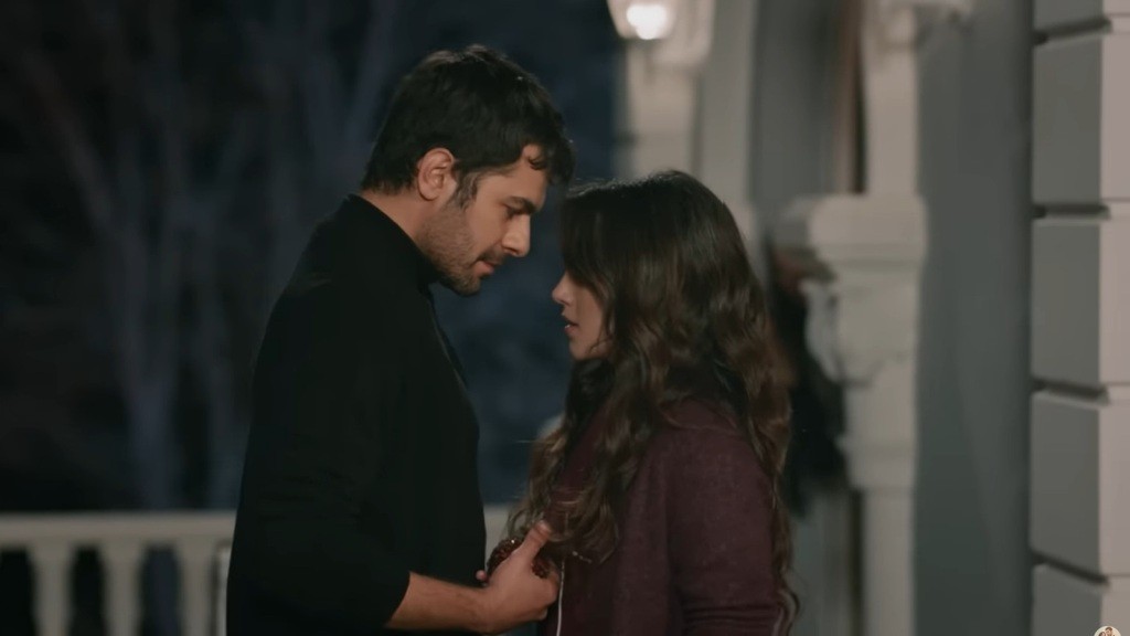 Halil bawi się włosami Zeynep, stojąc z nią twarzą w twarz na tarasie.