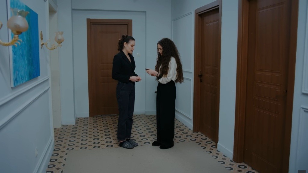 Nana trzyma w ręku telefon, stojąc przed Pelin.