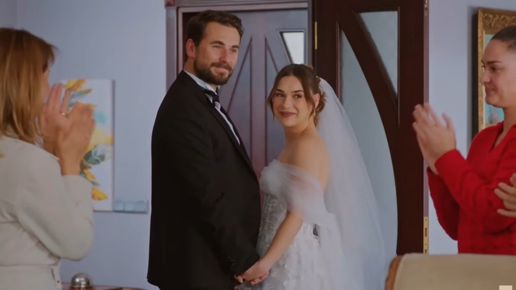 Kuzey i Sila stoją naprzeciwko siebie, trzymając się za ręce. Patrzą na gości, którzy biją im brawo.