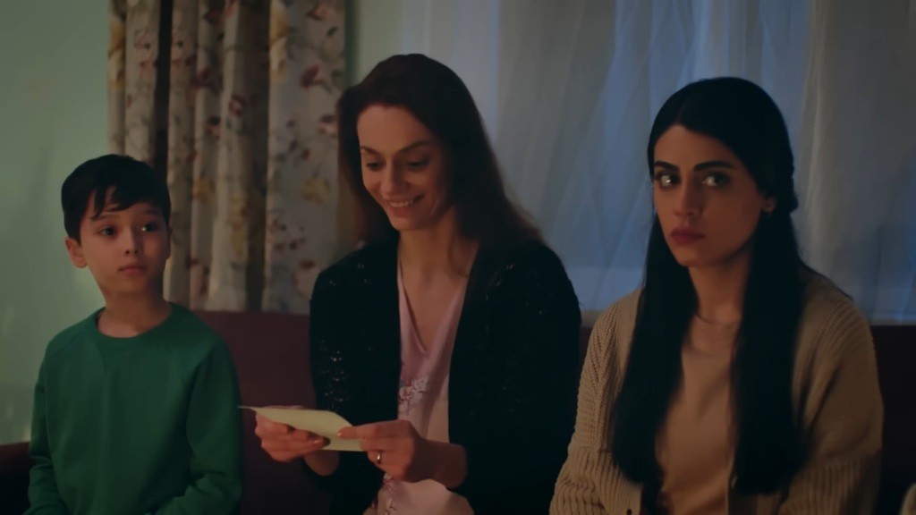 Derya trzyma w rękach zdjęcie i wpatruje się w nie z uśmiechem Obok niej siedzą Emir i Hancer.