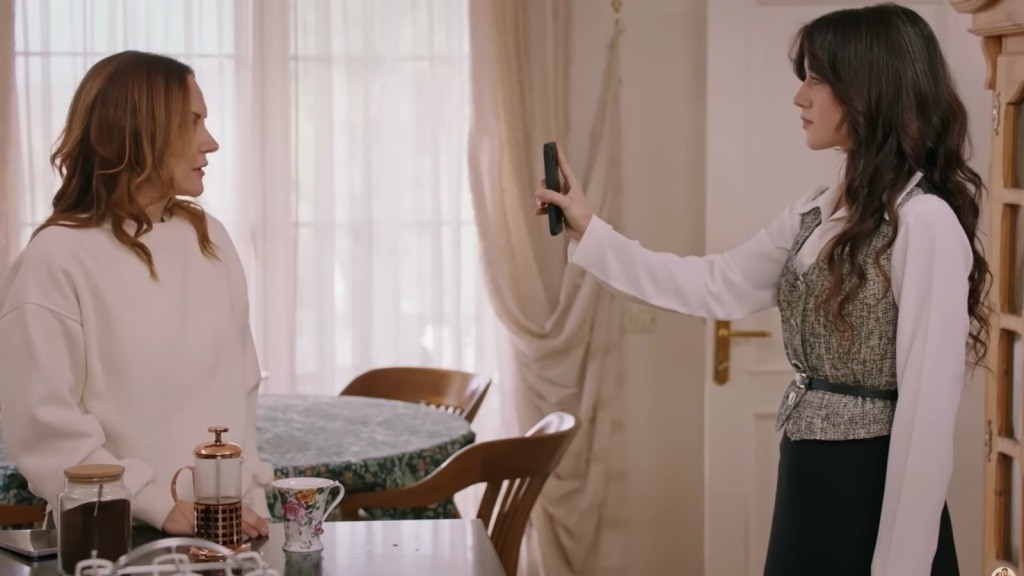 Zeynep stoi przed Songul, trzymając w ręku wyciągnięty telefon.