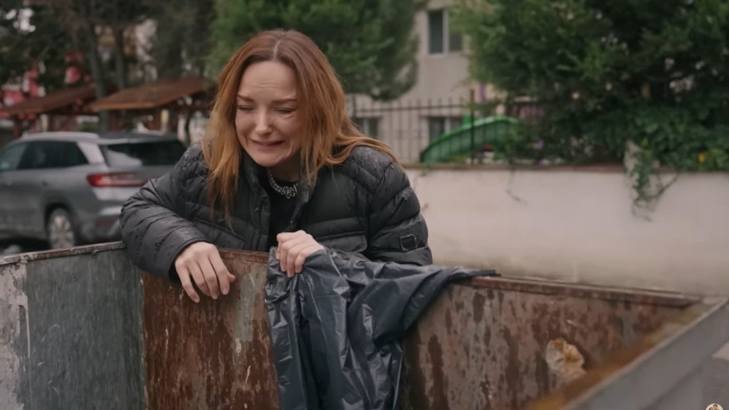 Zrozpaczona Songul pochyla się nad brudnym kontenerem na śmieci.