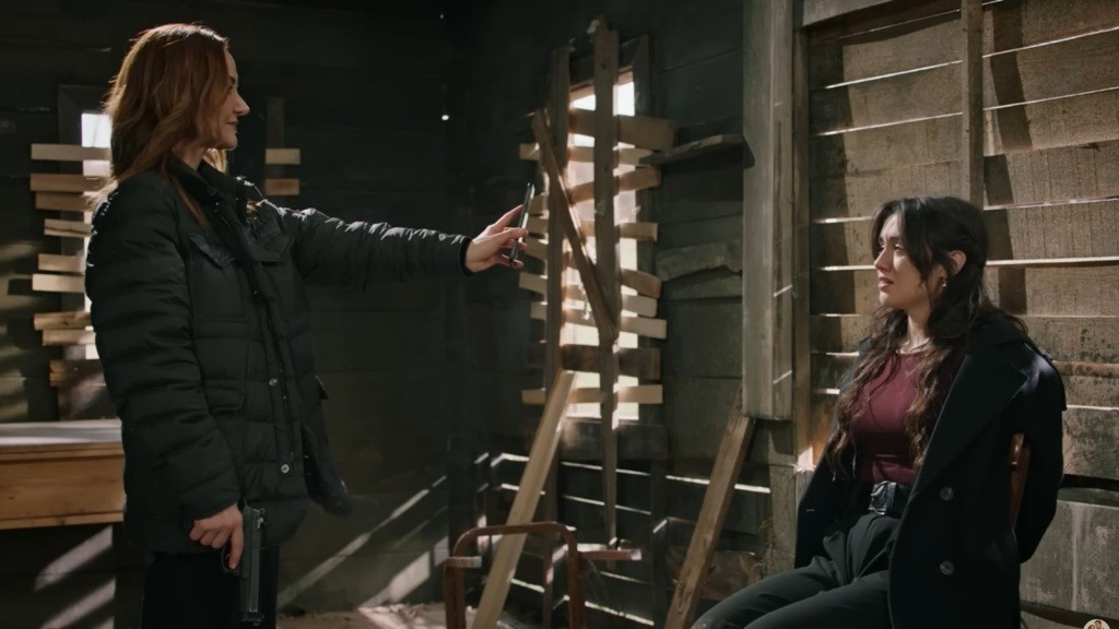 Songul stoi przed Zeynep z wyciągniętym przed siebie telefonem.