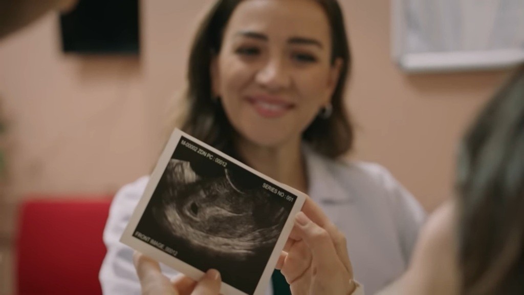 Zbliżenie na zdjęcie ultrasonograficzne. W tle widać uśmiechniętą twarz lekarki.