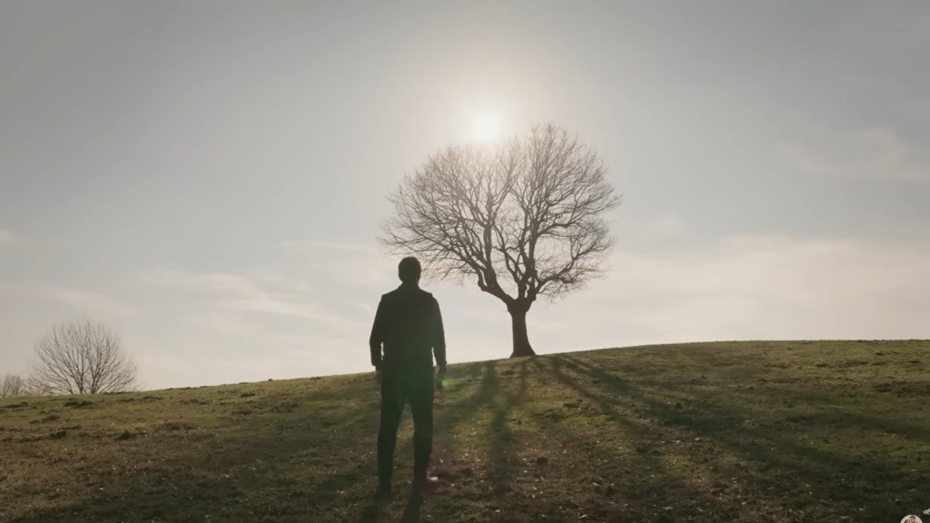 Halil stoi przed drzewem na wzgórzu.