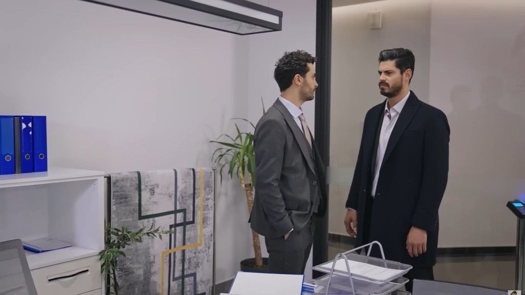 Engin i Cihan rozmawiają w firmie. Engin stoi przed Cihanem, trzymając ręce w kieszeniach.