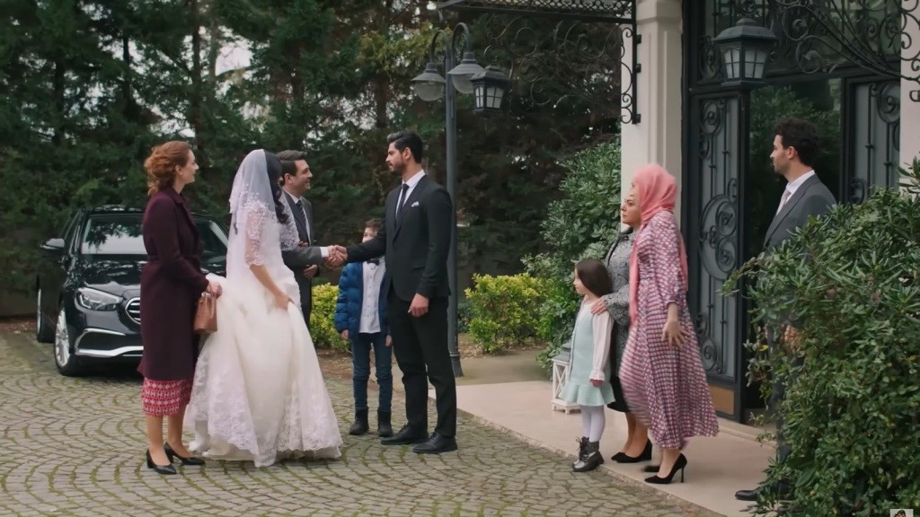 Cihan wymienia uścisk ręki z Cemilem, bok którego stoi Hancer w sukni ślubnej, a tuż za nią Derya.