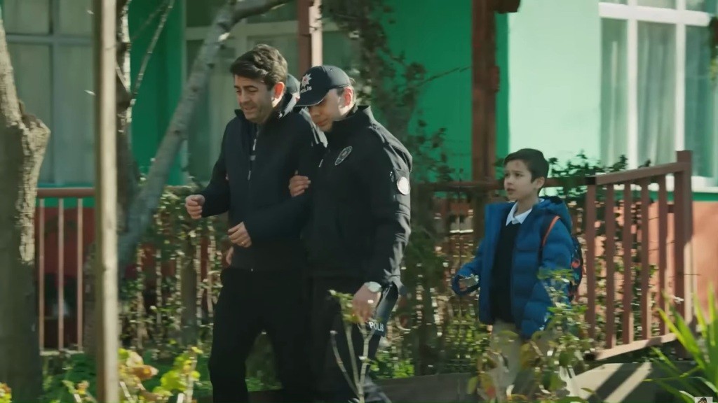 Policjanci prowadzą zatrzymanego Cemila. Mały Emir podąża za nimi.