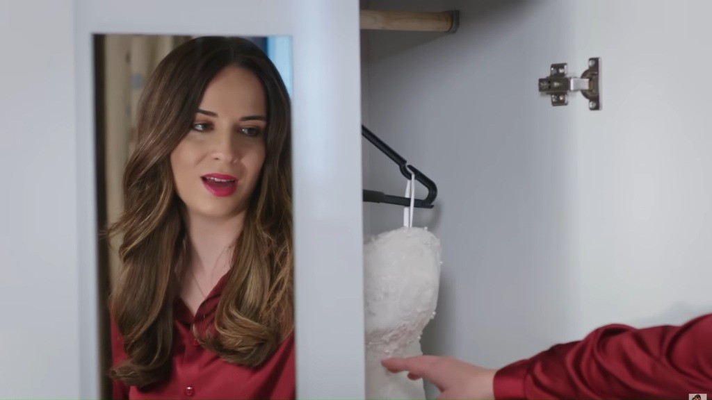 Derya dotyka wiszącej w szafie sukni ślubnej Hancer. Jej odbicie w lustrzanych drzwiach ukazuje subtelny blask emocji.