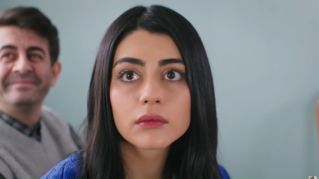 Hancer spogląda z zaskoczeniem. Za jej plecami siedzi Cemil i uśmiecha się.