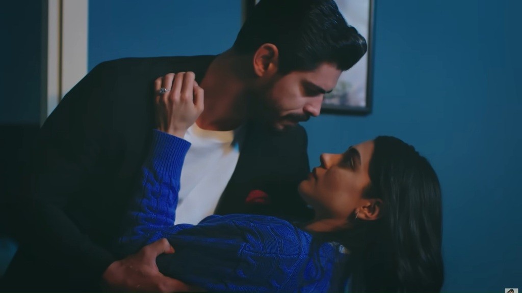 Cihan obejmuje Hancer, pochylając się razem z nią, jakby tańczyli. W pomieszczeniu panuje półmrok.