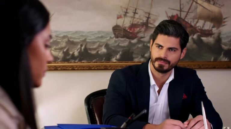 Cihan, siedząc za swoim biurkiem, przygląda się Hancer.