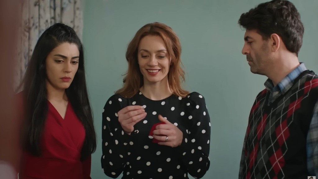 Derya trzyma w rękach czerwone pudełeczko i pierścionek. Uśmiecha się. Hancer i Cemil stoją obok niej.