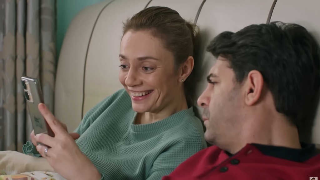 Derya śmieje się, wpatrzona w ekran telefonu. Cemil zerka z zainteresowaniem.