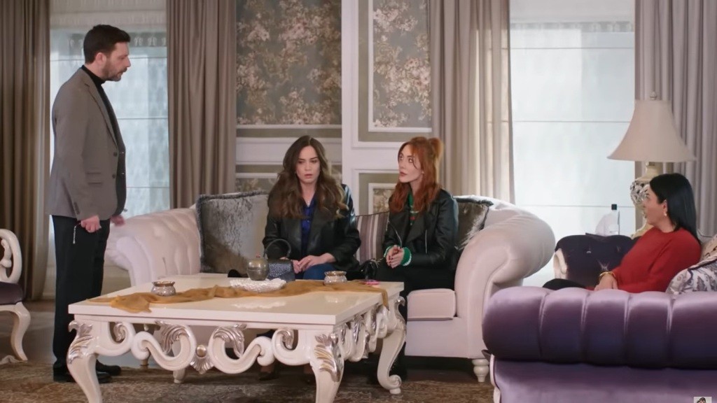 Nusret stoi. Beyza i Yonca siedzą obok siebie na kanapie. Na drugiej kanapie siedzi Mukadder.