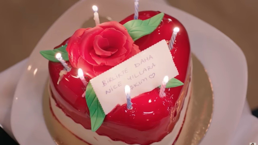 Czerwony tort w kształcie serca z siedmioma świeczkami i karteczką.